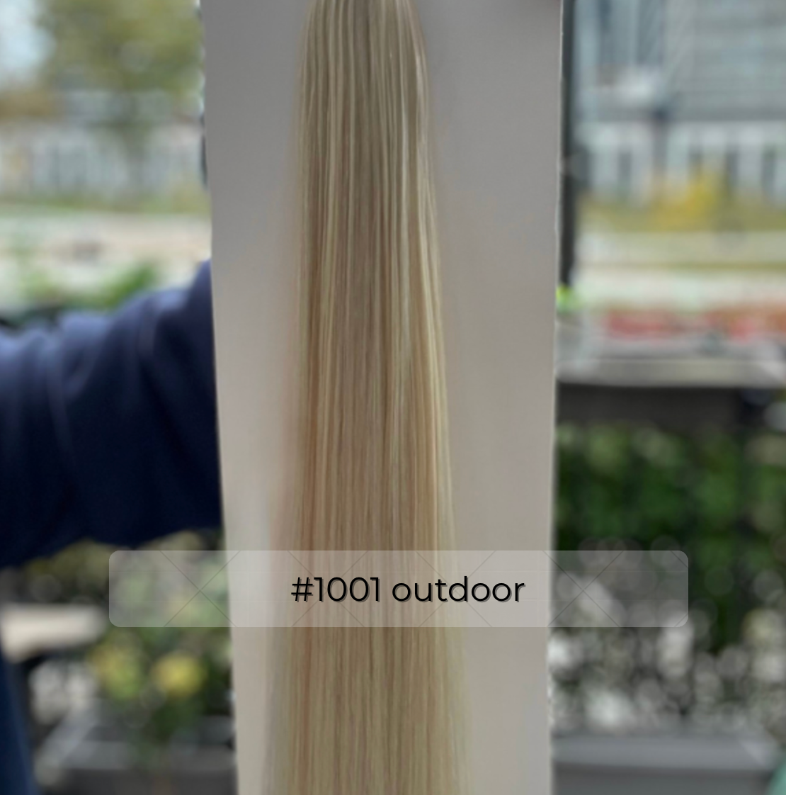 Platinum blonde #1001 tape in hair extensions in natural outdoor light, straight strand showing icy-platinum shine