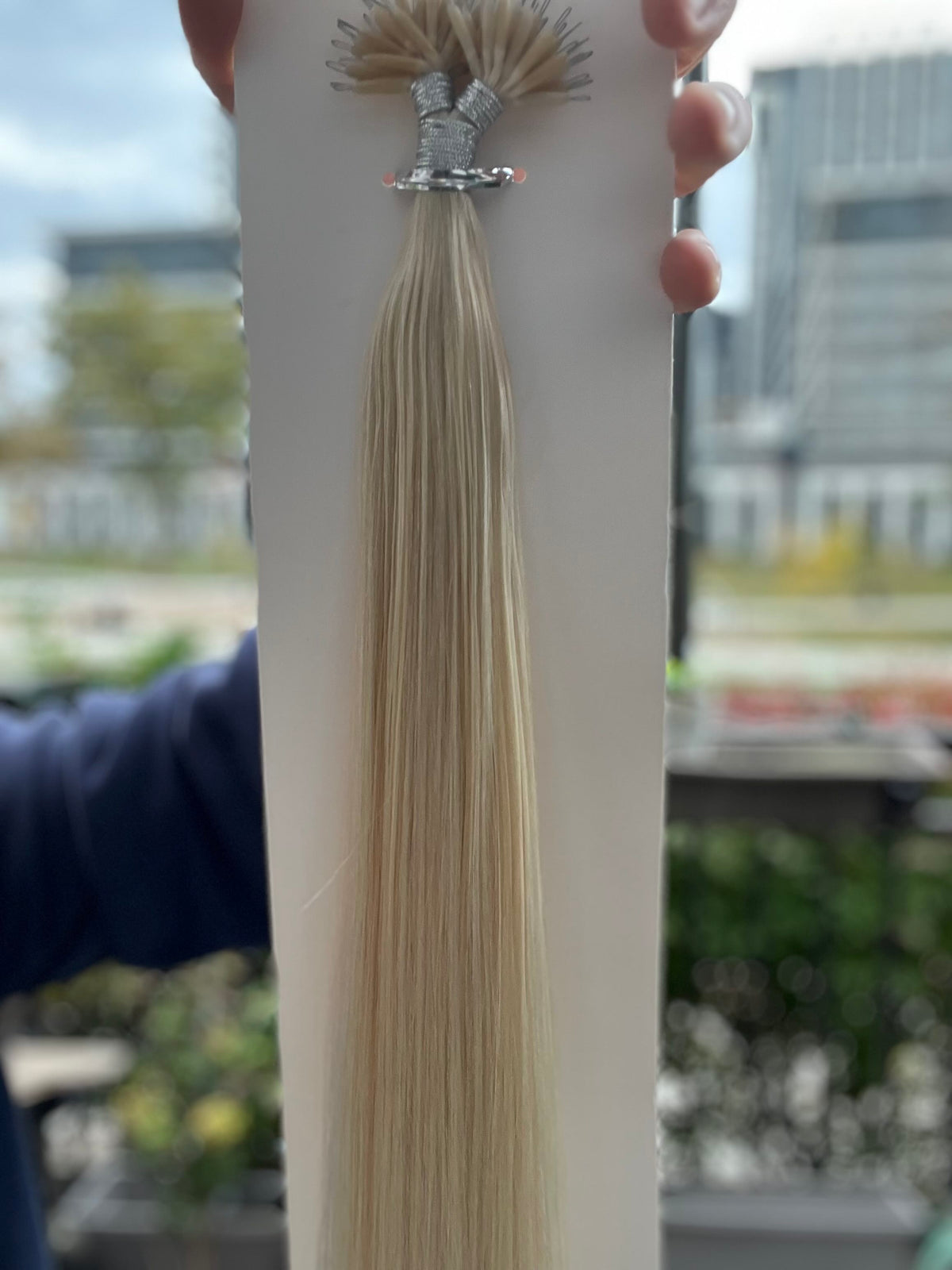 Hand holding card of straight platinum blonde #1001 nano bead hair extensions outdoors, nano rings at top