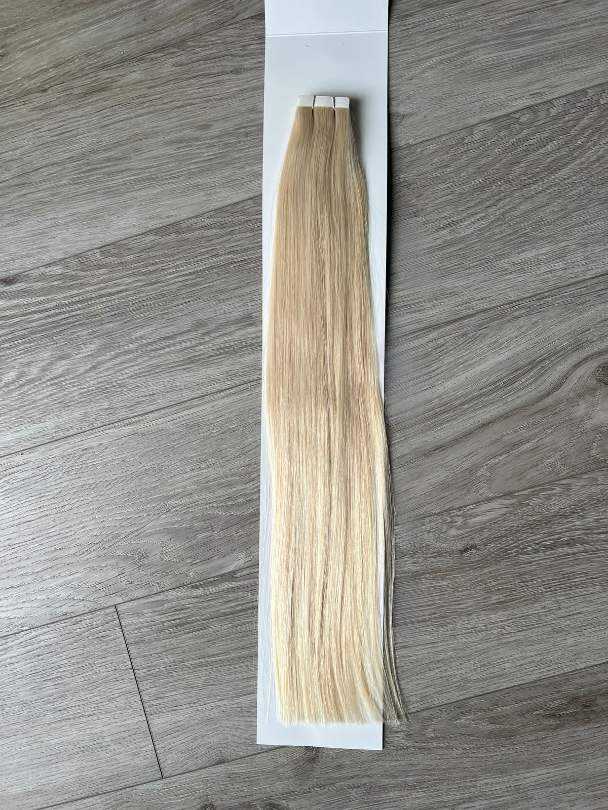 Single platinum blonde #1001 tape in hair extension weft with adhesive tape tab on wooden surface